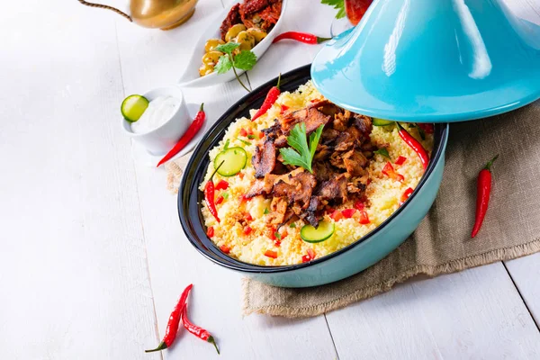 Beyaz arka planda kuskus, sebze ve etli Tajin.