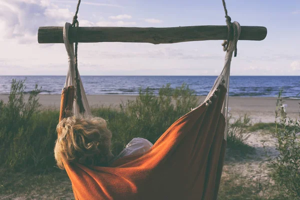 Woman resting in an orange lounge chair in the dunes on the Baltic Sea in the evening. Jurmala