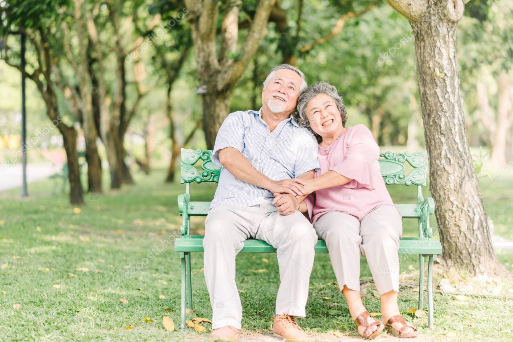 Happy Asian Senior couple sitting on the bench in the park enjoy a good time together