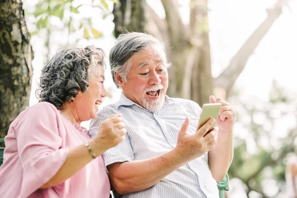 Mutlu üst düzey Asya çift gülüyor ve parkta otururken mobil smartphone içinde bir şey ile heyecan verici