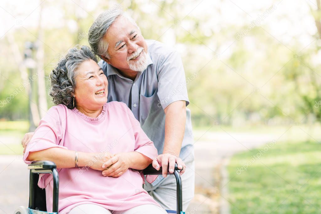 Happy Asian senior couple smiling outside in the park while woman sitting in wheelchair