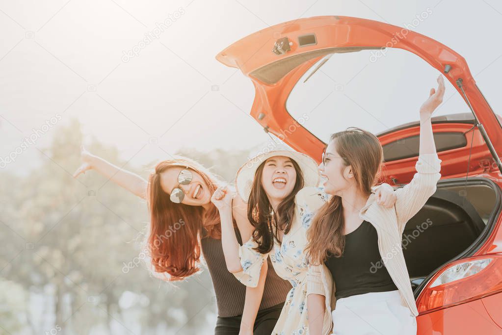 Three happy Asian girl best friends traveler celebrating a good time with arm up while sitting in car trunk 