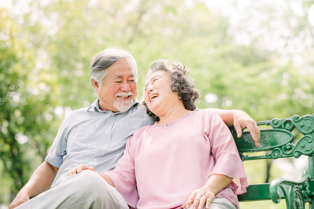 Happy Asian Senior couple laughing while sitting on the bench in the park 