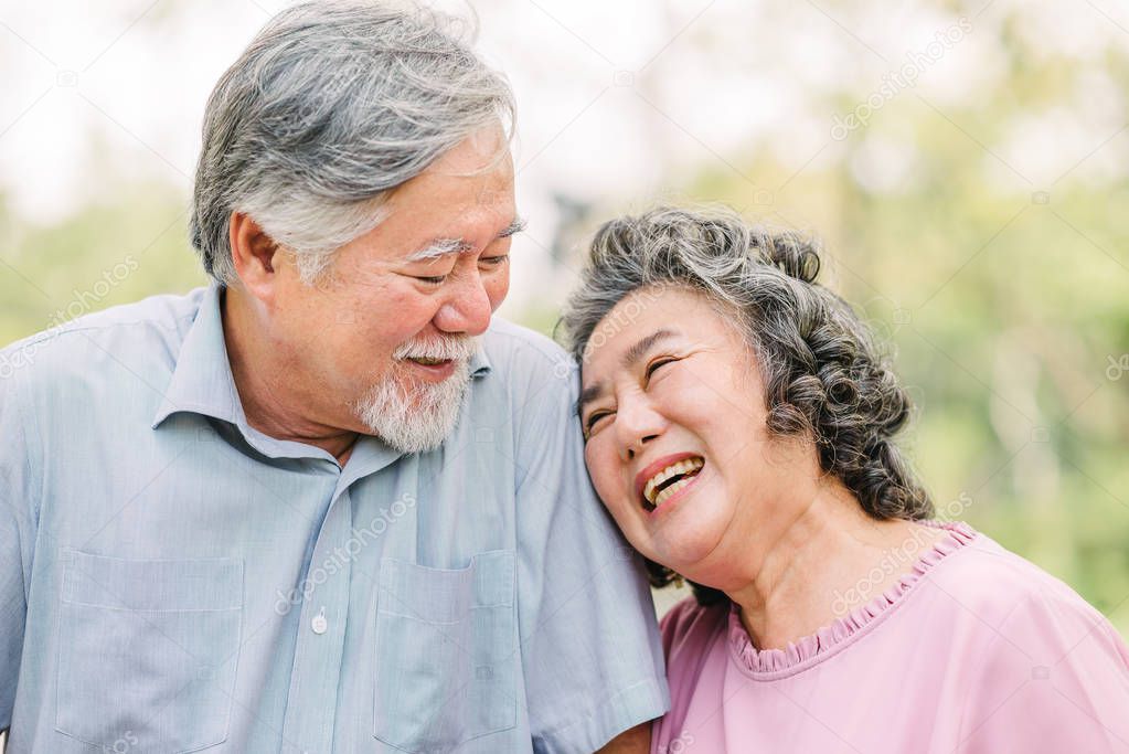 Happy Asian senior couple having a good time. They laughing and smiling while sitting outdoor in the park.
