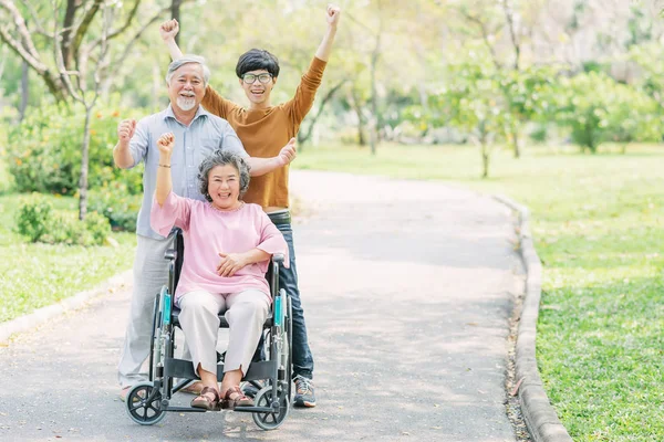 Happy family with senior woman in wheelchair in the park — Stock Photo, Image