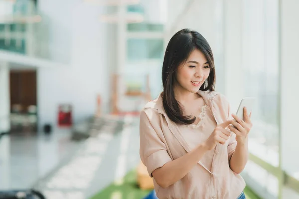 Mujer sonriendo mientras usa el teléfono inteligente en la oficina moderna —  Fotos de Stock