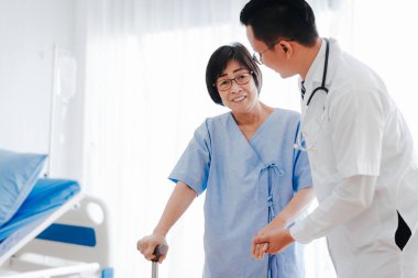 Doktor yaşlı kadına bastonla yardım ediyor. 