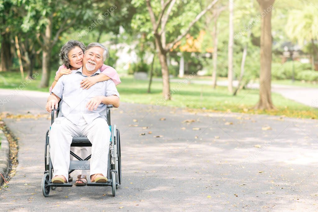 senior woman hugging her husband in wheelchair from behind 