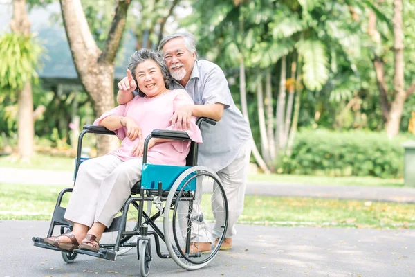 Mulher idosa feliz em uma cadeira de rodas andando com o marido — Fotografia de Stock