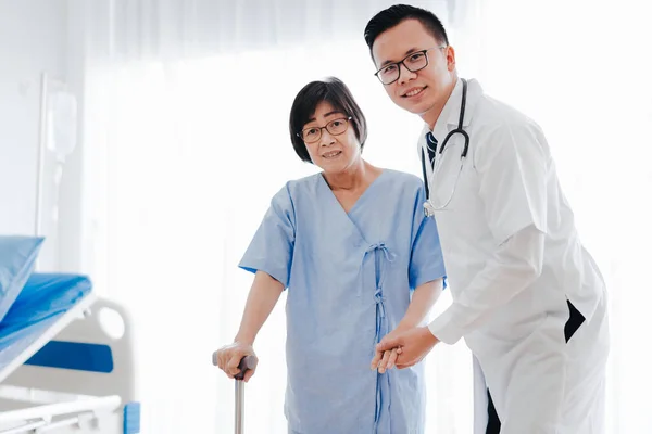 Médico ajudando a mulher idosa andando com uma bengala — Fotografia de Stock