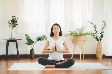 Çekici, sağlıklı bir Asyalı kadının oturma odasında yoga meditasyonu yapması.