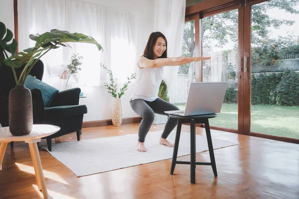 Mutlu Asyalı kadın evde dizüstü bilgisayardan egzersiz yapmayı öğrendi. COVID-19 sırasında evde kişisel izolasyon ve egzersiz