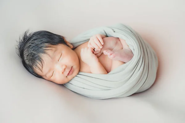 Sevimli, gülümseyen Asyalı bir bebek örülmüş bir şapka takıyor ve koza ile sarılıp yatakta uyuyor.
