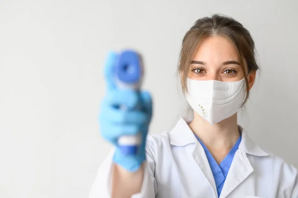 Female doctor wearing protective mask using infrared thermometer to check body temperature on white background