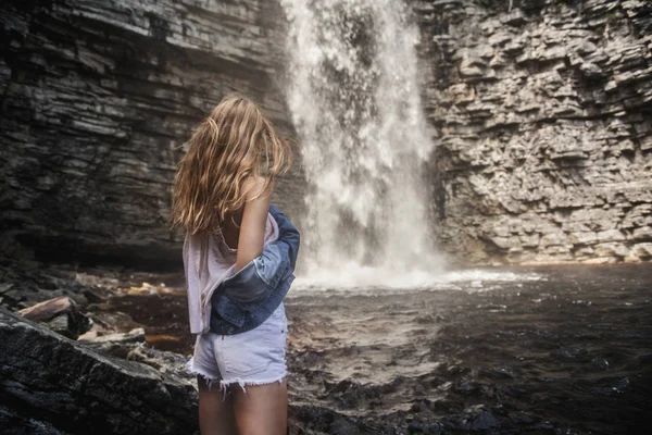 Beautiful model girl with long legs posing near a waterfall wearing jeans jacket