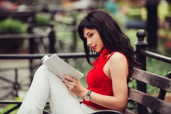 聪明漂亮的女人读一本书坐在公园的长凳上 — 图库照片