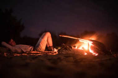 Kamp ve yangın yakınındaki plajda gece yalan yapan erkek