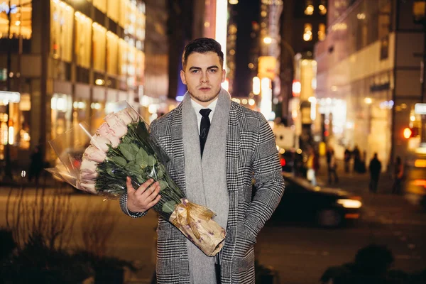 Handsome man walking to the date with rose flower bouquet at night city