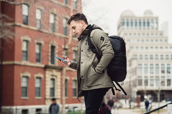 学生男子短信在手机走在城市大学校园与背包 — 图库照片