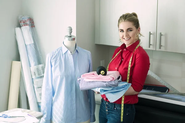 Tailor woman smiling in atelier design studio holding sewing tools