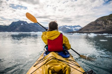Alaska 'da buzulları keşfetmek için buzlu bir körfezde kano süren bir kadın.