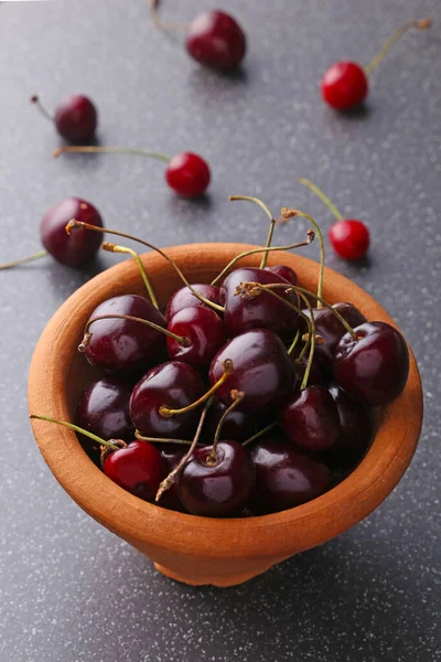 Fresh sweet cherries bowl with leaves in water drops on stone background, top view