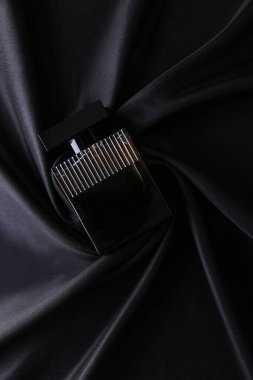 İpek katlanmış kumaş kaplama parfüm şişesinde parfüm şişesi. Karanlık, boş arka planda. Üst görünüm. 