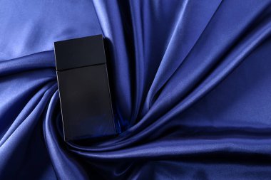 İpek katlanmış kumaş kaplamalı parfüm şişesi. Koyu mavi sıvılı cam matara. Kozmetik güzellik ürünü.