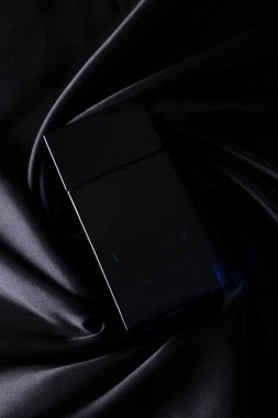 İpek katlanmış kumaş kaplama parfüm şişesinde parfüm şişesi. Karanlık, boş arka planda. Üst görünüm. 