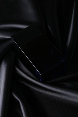 İpek katlanmış kumaş kaplama parfüm şişesinde parfüm şişesi. Karanlık, boş arka planda. Üst görünüm. 