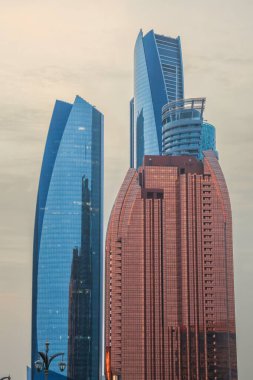 Abu Dabi, BAE 16 Ağustos 2025: Gökdelenler Birleşik Arap Emirlikleri 'nin başkentinde gün batımında fıskiyelerle dolu palmiye dolu bir parka bakıyor.