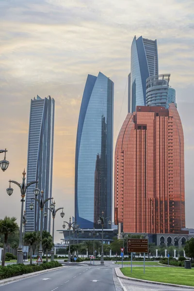 Abu Dabi, BAE 16 Ağustos 2025: Gökdelenler Birleşik Arap Emirlikleri 'nin başkentinde gün batımında fıskiyelerle dolu palmiye dolu bir parka bakıyor.