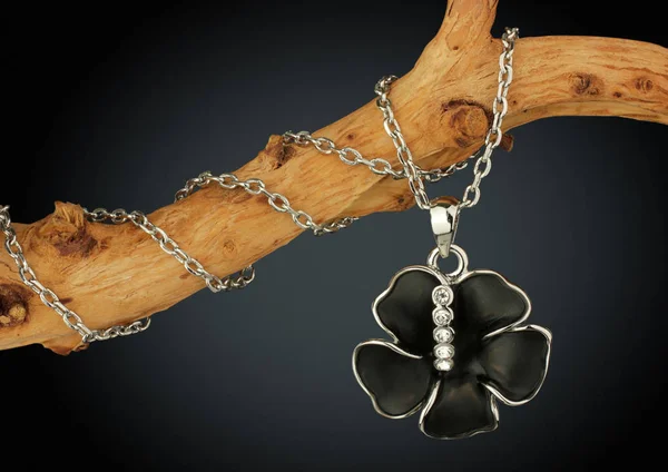 Jewelry pendant shape of black flover on twig, on dark backgroun — Stock Photo, Image