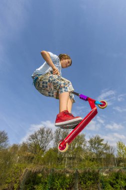 Çocuk bir scooter ile paten parc bir omurga üzerinden atlama ve zevk