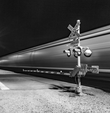 Railroad crossing with passing train by night clipart