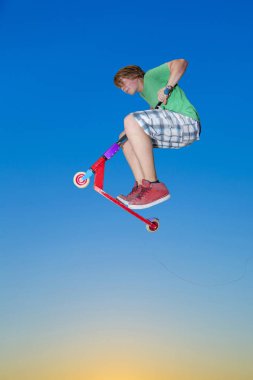 oğlan mavi gökyüzü altında onun itme scooter ile atlama