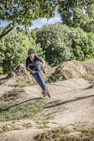 Menino monta seu empurrar scooter em um parque de bicicleta — Fotografia de Stock