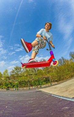 oğlan bir scooter ile bir omurga skate Park üzerinden atlıyor