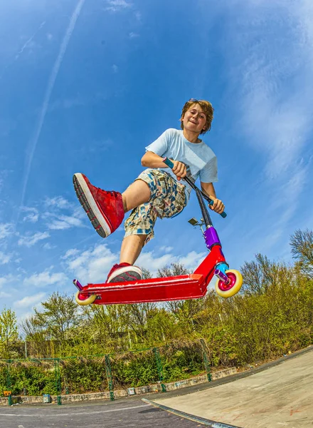 Мальчик прыгает на скутере через хребет в скейт-парке — стоковое фото