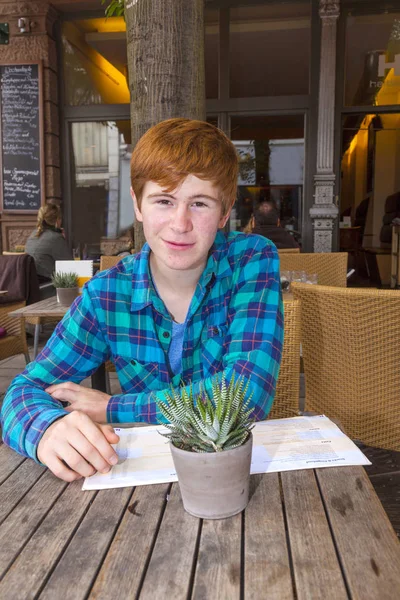 Young teenage boy with red hair sitting in an outdoor restauran — Stock Photo, Image