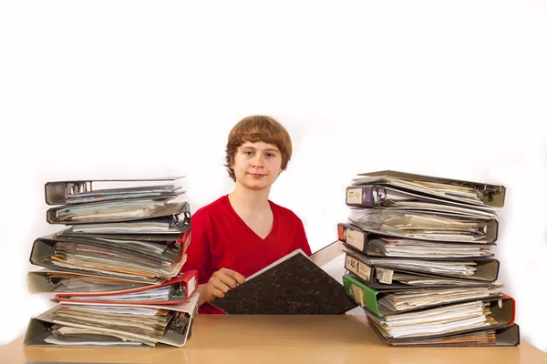 Teenage Boy sentado em uma mesa com muitas pastas e leitura — Fotografia de Stock