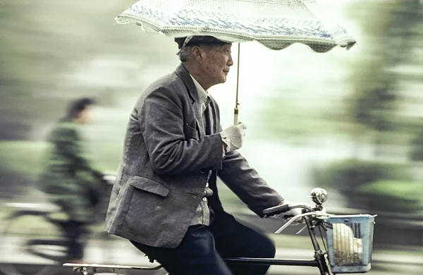 Yaşlı adam kolunda şemsiyeyle bisiklete biniyor. — Stok fotoğraf