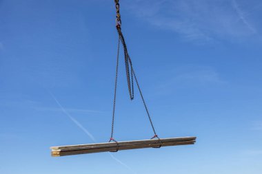 Mavi gökyüzünün altında bir vincin kancasındaki kalaslar