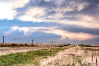 A remote roadway in the Great Plains in Tornado Alley shows a very subtle sunset along a grassy lines road as the pink sun sets for the day clipart