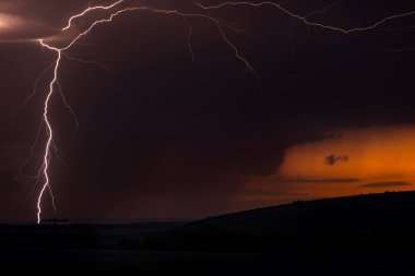 A large lightning strike at dusk in an open plain framed against a deep, dark orange sunset and stormy skies. clipart