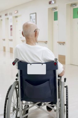 Eski hastane koridorunda tekerlekli sandalye üzerinde oturan adam arkadan görünüm