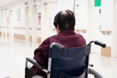 Hastanede tekerlekli sandalye üzerinde oturan üst düzey veya yaşlı kadın arkadan görünüm                                 