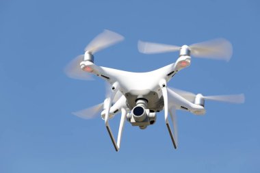 Beyaz dron havada uçuyor ve arka planda açık mavi gökyüzü