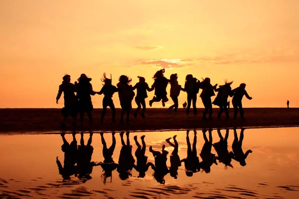 Silhouette of young women on a sunset beach. Jumping young girls with reflection on the beach