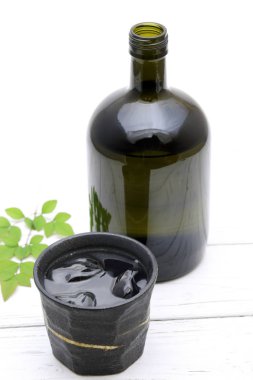 Ahşap beyaz masa üzerinde Japon shochu ve seramik kase Şişe